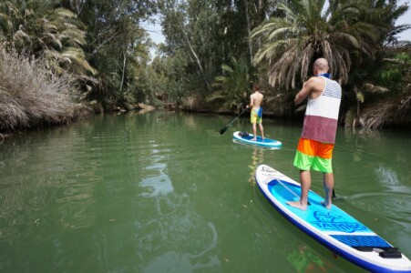 Two SUP riders on blue water and palm trees on the banks
