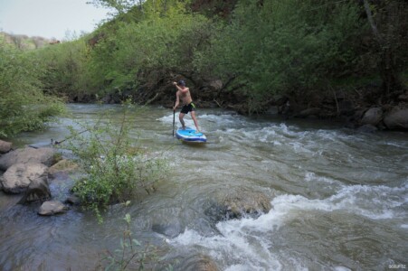 Narrow river with green vegetation and paddleboardist in the middle