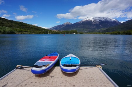 Two paddleboards and two paddles next to a lake under mountains